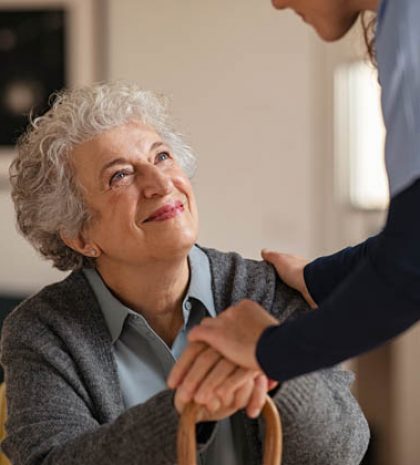 Old woman talking with a female doctor while holding hands at home. Smiling senior woman talking to her general practitioner visiting her at home during virus epidemic. Happy old patient holding hands of caregiver at nursing home.